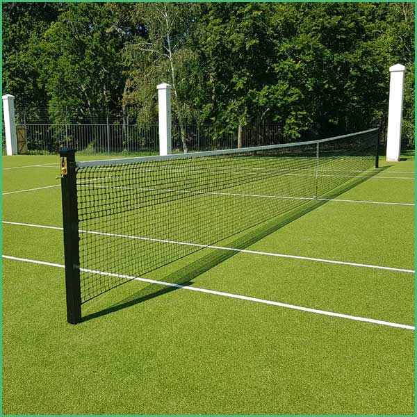 Outdoor tennis court with a net stretched across the green surface, white boundary lines, and a fence with trees in the background