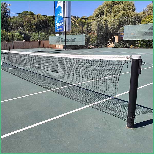 Outdoor hard tennis court with a net in the foreground and banners in the background under a clear sky