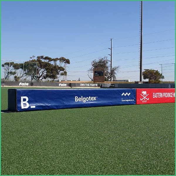 Padding barrier on a sports field with Belgotex ad, artificial turf in the foreground and trees in the background