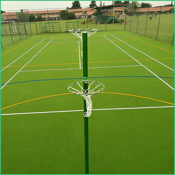 Outdoor multi sport court with a tall green pole and two white circular net hoops attached, viewed from the center