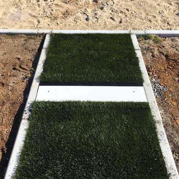 Concrete bordered artificial turf stepping stones forming a narrow path on a construction site, with bare dirt around 