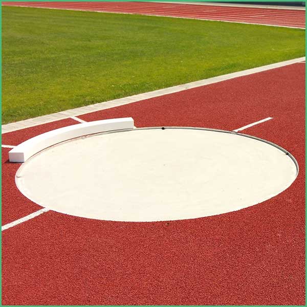 Empty shot put throwing circle on a red track with a green field in the background