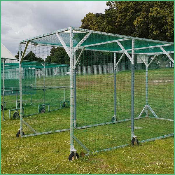 Portable metal framed fencing enclosure on wheels with wire mesh panels and a green roof, set up on a grassy field