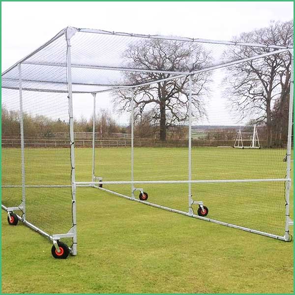 Portable metal baseball batting cage on wheels set up on a grassy field, with netting and trees in the background