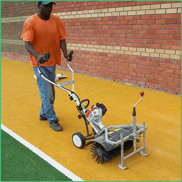 Worker in an orange shirt operates a line marking machine to paint a yellow track line against a brick wall outside