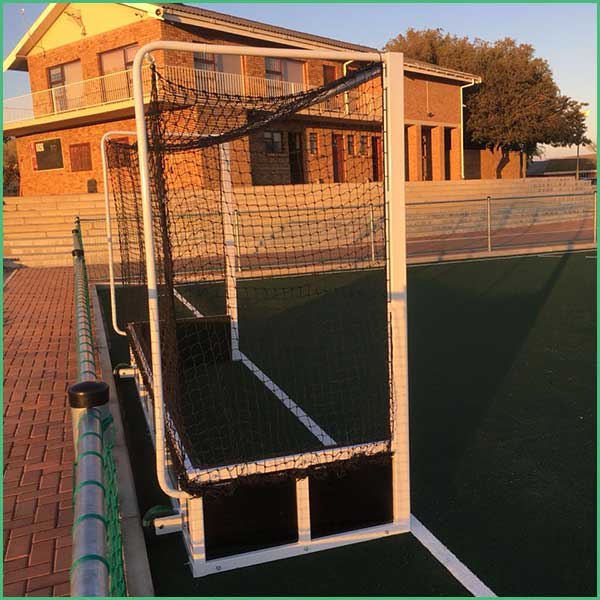Portable soccer goal with net on an artificial turf field near a brick building and fence in the background