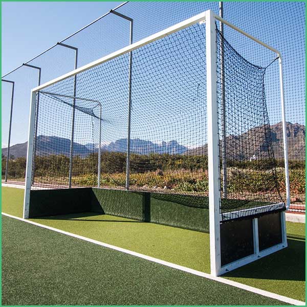 Soccer goal enclosed by protective netting on an artificial turf field with mountains in the background