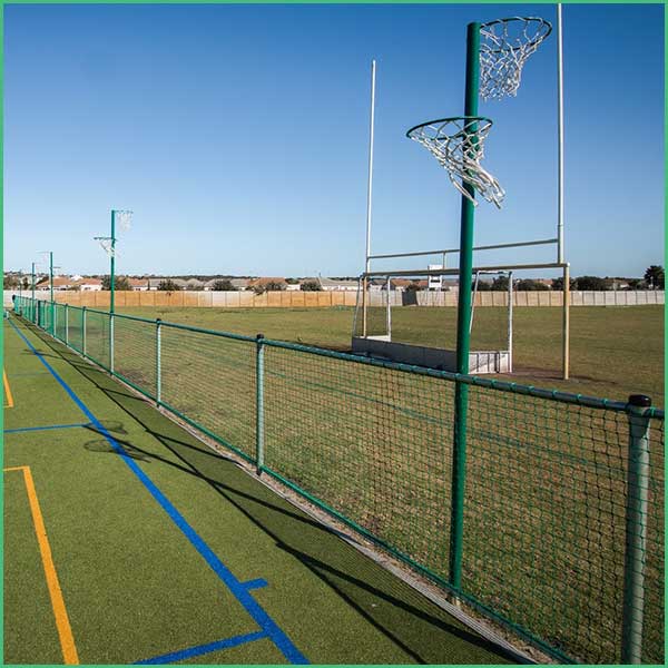 Outdoor basketball court with two hoops and a green chain link fence along a grassy field under a clear blue sky