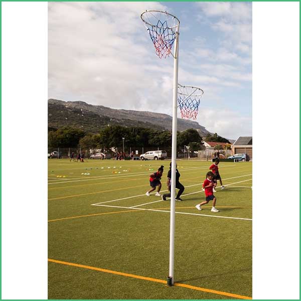 Children playing on an artificial turf field with two basketball hoops nearby and hills in the background of a wide park scene