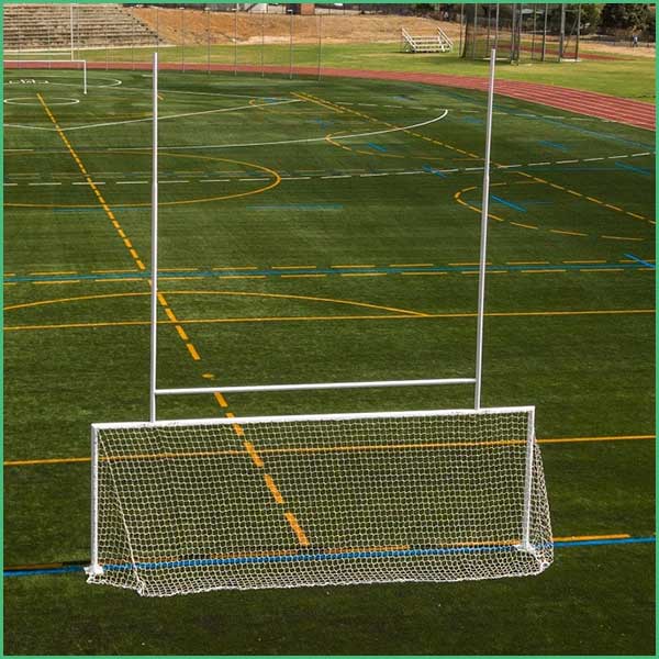 White soccer goal on artificial turf with yellow and blue field lines, and tall posts behind the net