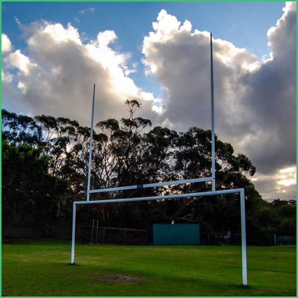 Rugby goalposts on a grassy field with a blue sky and trees behind