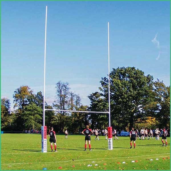 Rugby goalposts on a grassy field with players in black jerseys and red socks nearby; spectators in the background 