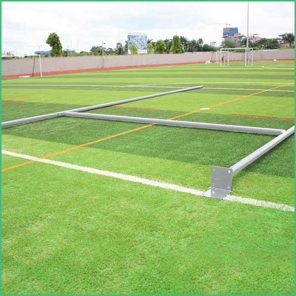 Metal frame supports laid out on a synthetic turf field during construction; goalposts visible in the distance and white boundary lines in view 