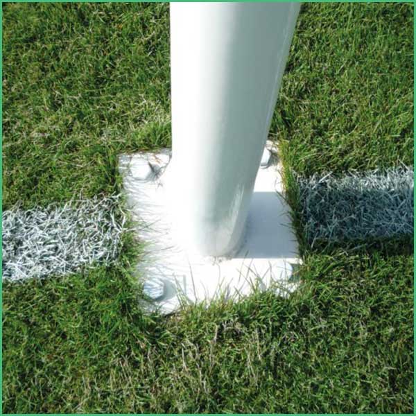 White flagpole mounted on a square concrete footing anchored in a grassy lawn, with metal stabilizing sleeves on either side