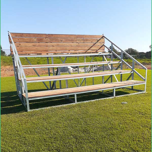 Outdoor metal and wood bleachers on a grassy sports field under a clear blue sky