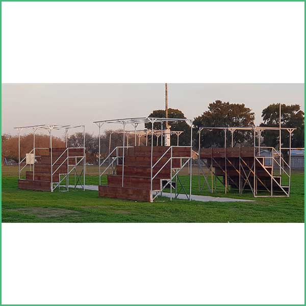 Outdoor obstacle course on a grassy field with wooden platforms and metal frames and stairs at dusk/sunset