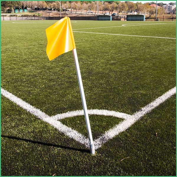 Yellow corner flag planted at the corner of a soccer field on green turf with white boundary lines visible in the foreground