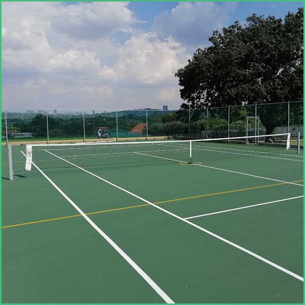 Outdoor tennis court with a net, white boundary lines, and a green surface enclosed by a chain link fence and trees in the background