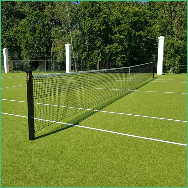 Tennis net on a bright green outdoor court with white boundary lines and trees in the background