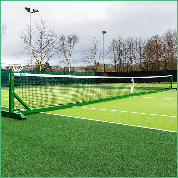 Outdoor tennis court with a green net and leafless trees in the background under a cloudy sky on a sunny day? No, it’s an outdoor court with a net across and green surface