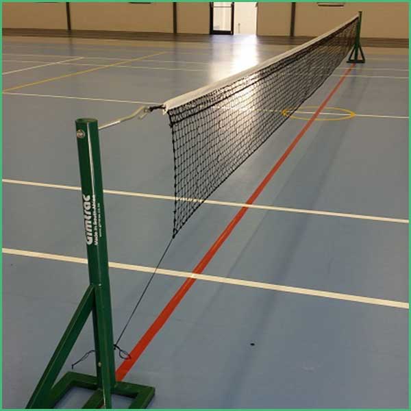 Portable badminton net set up in a gymnasium on a blue floor with white and red court lines visible
