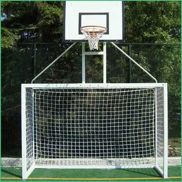 Basketball hoop mounted above a large white soccer goal with a net, on a fenced outdoor court