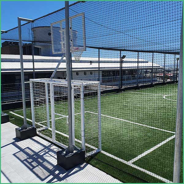Rooftop sports court with a small soccer goal and protective netting surrounding the field