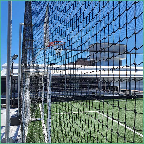 Basketball hoop seen through a chain link fence on an outdoor court, with a building in the background