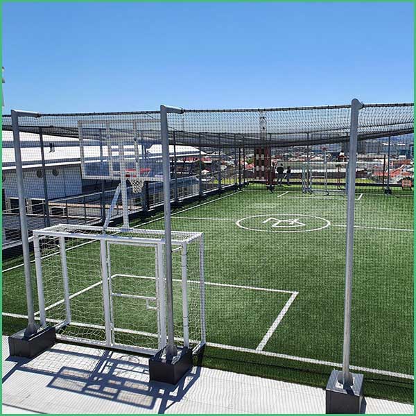 Rooftop mini soccer pitch with artificial turf, white boundary lines, and safety netting; gate in foreground
